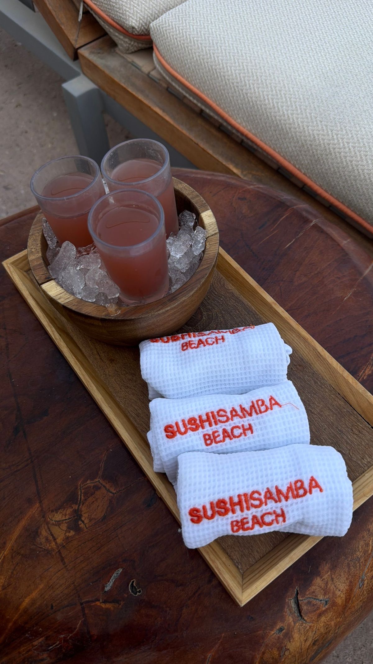 Chilled drinks and rolled towels on a wooden tray at a beach club