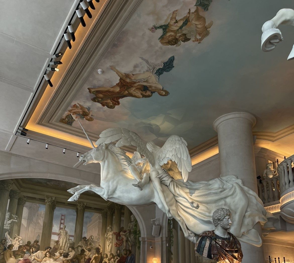 A grand dining room with a painted ceiling and a winged marble sculpture