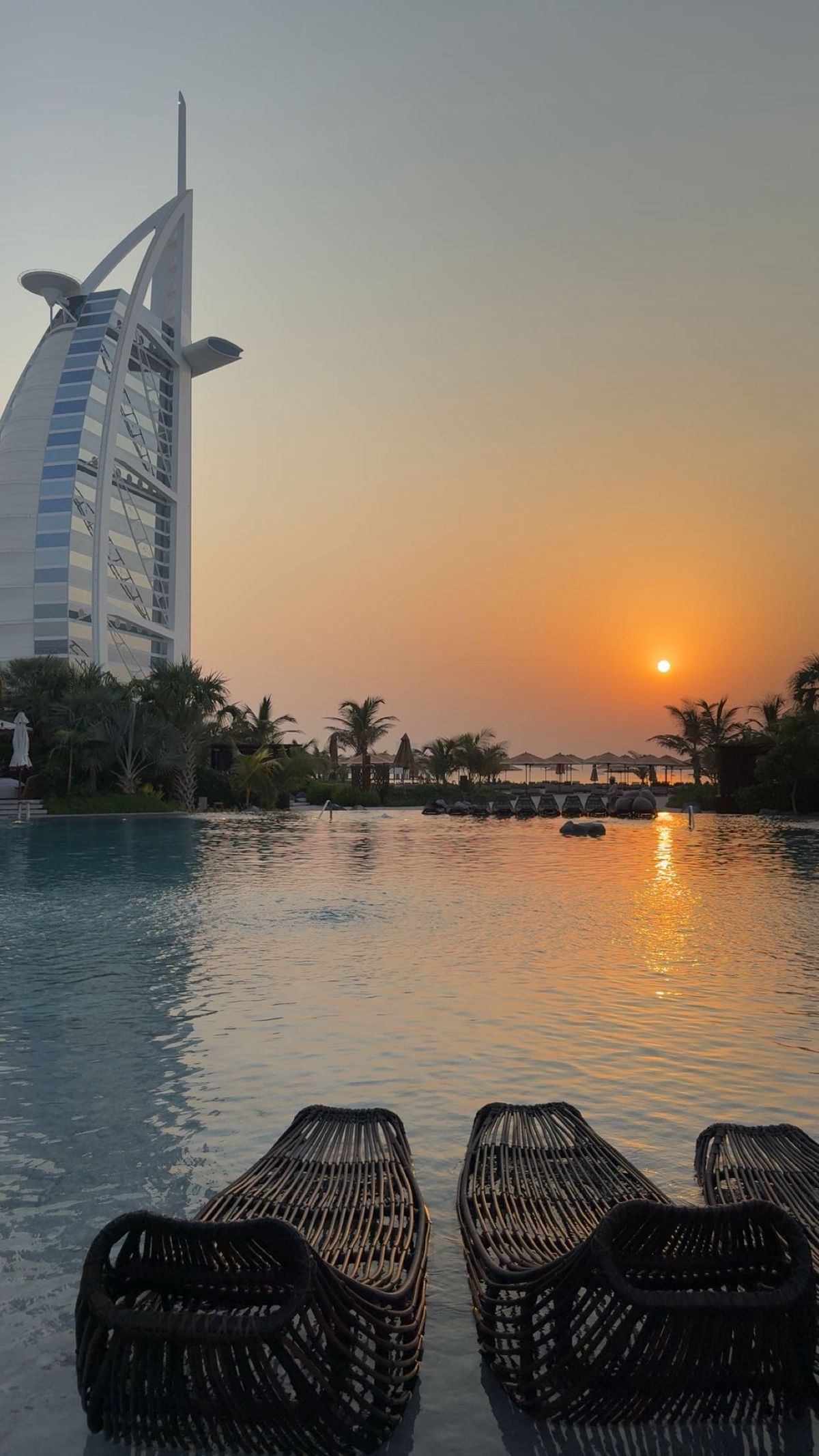 A resort pool at sunset beside a sail-shaped hotel tower